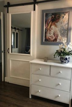 a white dresser sitting in front of a mirror on top of a wooden floor next to a doorway