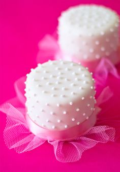 two white cakes sitting on top of a pink cloth covered cake plate with polka dots