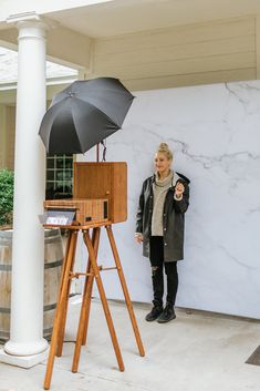 a woman standing in front of a white marble wall holding an umbrella and looking at the camera