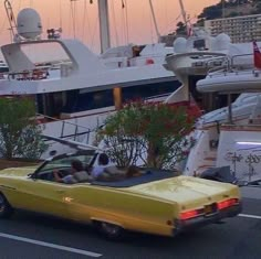 a yellow convertible car driving down a street next to yachts and boats in the water