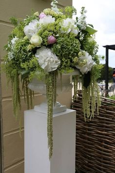 a tall white vase filled with flowers next to a basket on the side of a building