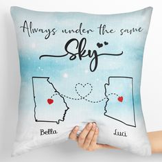 someone holding up a pillow that says, always under the same sky with two hearts