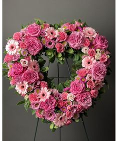 a heart - shaped wreath with pink flowers on a stand in front of a gray background