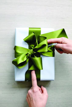 a person pointing at a present wrapped in green satine with a bow on it