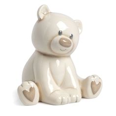 a white ceramic teddy bear sitting on the ground with its paws in the shape of a heart