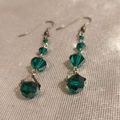 the green earrings are hanging from silver earwires on a white cloth surface, with small beads attached to them