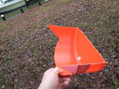 a hand holding an orange plastic boat in the grass