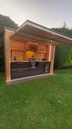 an outdoor kitchen is built into the side of a grassy area with trees in the background