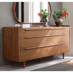 a wooden dresser with two vases on top and a mirror in the corner above it