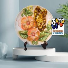 a ceramic plate with flowers and butterflies on it sitting on a stand next to a potted plant