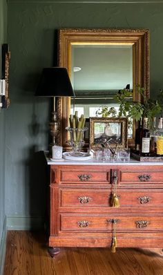 an old dresser with many bottles and glasses on it in a room that has green walls