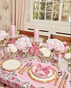 the table is set with pink and white flowers, plates, silverware and candles