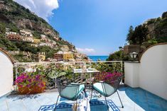 two chairs and a table on a balcony overlooking the ocean, with flowers in pots