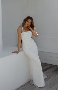 a woman in a white dress leaning against a wall