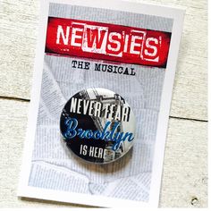 a button with the words newsies on it sitting on top of a piece of paper