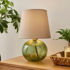 a green glass lamp sitting on top of a wooden table next to a potted plant