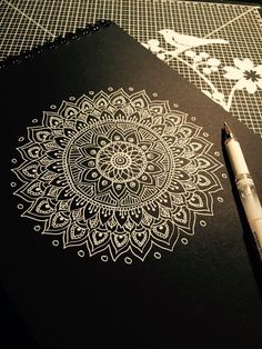 a pen sitting on top of a black notebook next to a drawing pad with white designs