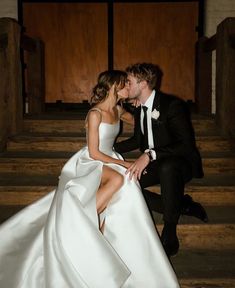 a bride and groom sitting on the steps in their wedding gowns, kissing each other