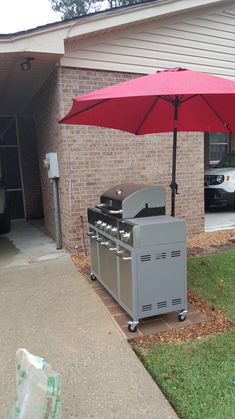 an umbrella that is open in front of a grill on the side of a house