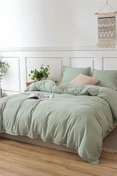 a bed with green sheets and pillows in a white room next to a potted plant