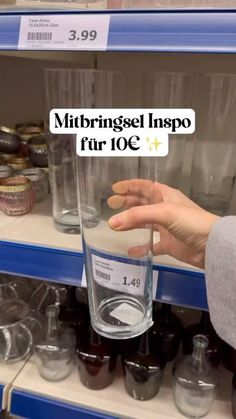 a person is holding a glass in front of some cups on the shelf at a store