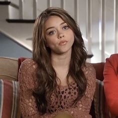 two women sitting next to each other on top of a red couch in front of stairs