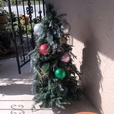 a small christmas tree with ornaments on it in front of a gated porch area