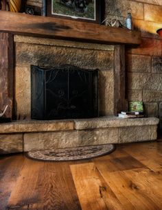 a stone fireplace with wood flooring in a rustic living room or dining room area