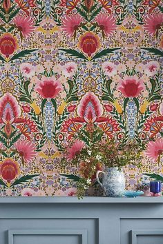 a vase with flowers on top of a blue table next to a wallpapered wall