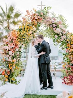 a bride and groom standing in front of a floral arch