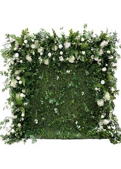 an arrangement of white flowers and greenery on top of a green square shape wall