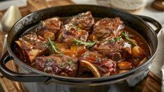 a pot filled with meat and vegetables on top of a wooden cutting board next to utensils