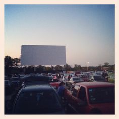 a lot of cars that are parked in front of a large screen on the side of a building