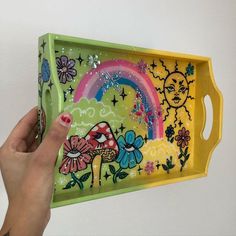 a hand holding a tray with an image of a mushroom and rainbow painted on it