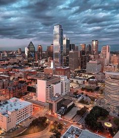 an aerial view of a city at dusk with clouds in the sky and buildings lit up