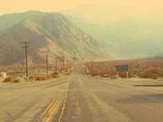 an empty road with mountains in the background and power lines on either side that run parallel to each other