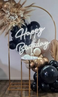 a happy birthday sign surrounded by black and gold balloons