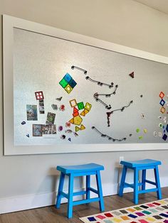 two blue stools are in front of a white wall with colorful artwork on it