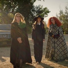 three women dressed up in costumes standing next to each other near a truck and trees