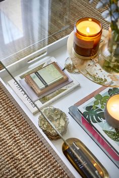 a tray with candles, books and other items on it next to a glass table