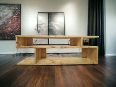 a wooden shelf sitting on top of a hard wood floor next to two pictures hanging on the wall