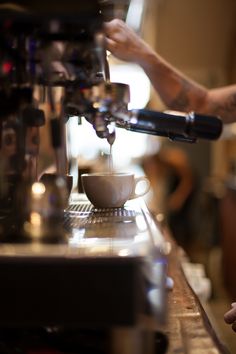 someone is pouring something into a cup at a coffee shop or cafe, with their hand on the espresso machine