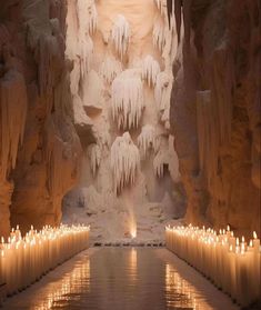 many candles are lit in front of an ice - covered cave with water and icicles on the walls