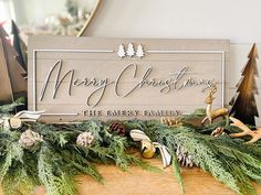 a merry christmas sign sitting on top of a wooden table next to evergreen branches and pine cones