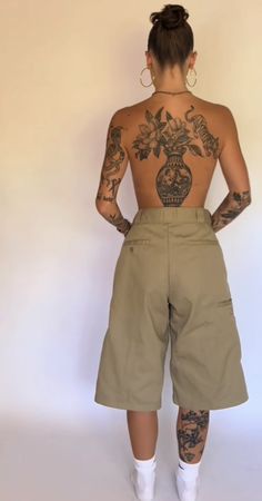 the back of a woman with tattoos on her body and wearing khaki shorts