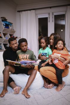 a group of people sitting on top of a bed reading a book and smiling at the camera