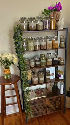 a shelf filled with jars and flowers next to a wooden stool on top of a hard wood floor