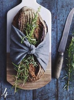 a cutting board topped with a loaf of bread covered in herbs next to a knife