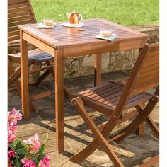 a wooden table with two chairs and a tea pot on top of it next to flowers