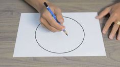 someone is drawing a circle on paper with a pen and pencil in front of them